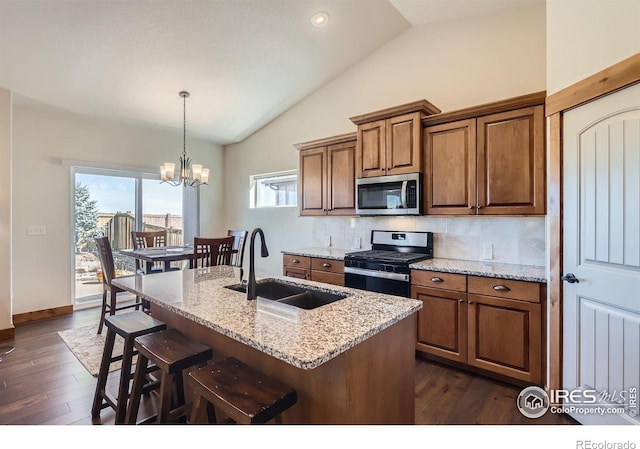 kitchen with lofted ceiling, stainless steel appliances, a sink, brown cabinets, and light stone countertops