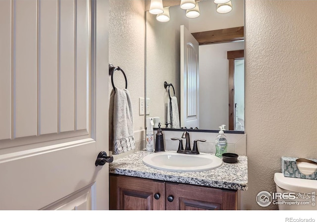 half bathroom with a textured wall, vanity, and toilet