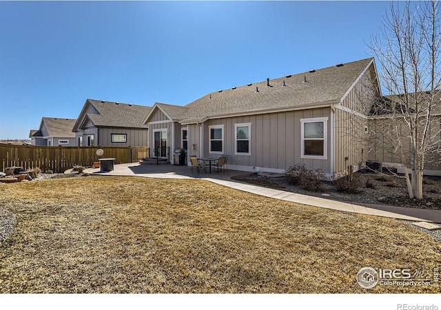 rear view of house featuring a lawn, a patio, roof with shingles, fence, and board and batten siding