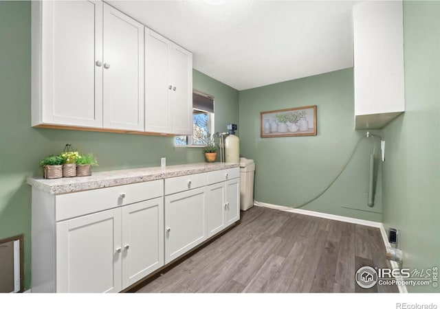 laundry area with light wood finished floors, baseboards, and cabinet space