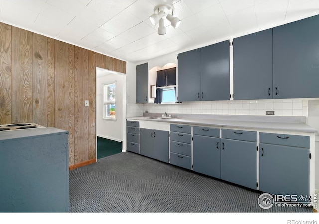 kitchen featuring wooden walls, a sink, light countertops, blue cabinetry, and backsplash