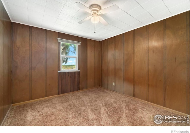 carpeted empty room with wood walls and a ceiling fan