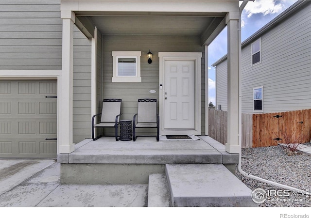 view of exterior entry featuring a garage, covered porch, and fence