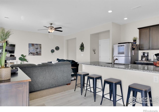 kitchen with a breakfast bar, a sink, dark brown cabinets, freestanding refrigerator, and light wood finished floors