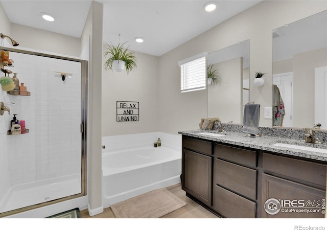 bathroom with a stall shower, double vanity, a sink, and a bath