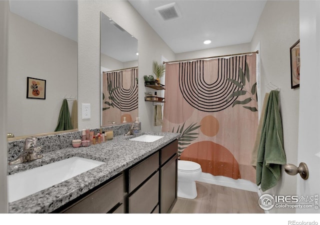 bathroom featuring toilet, visible vents, a sink, and wood finished floors