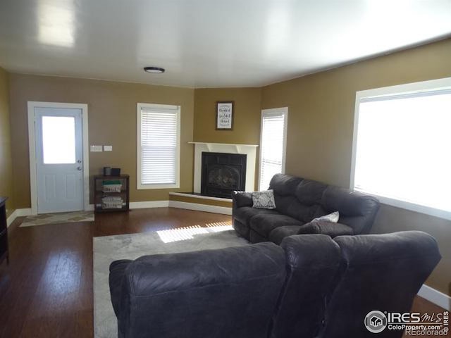 living area with a fireplace with raised hearth, dark wood finished floors, and baseboards