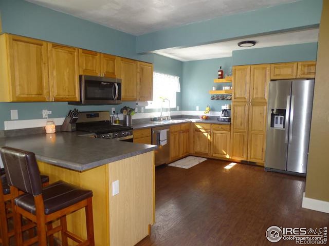 kitchen featuring stainless steel appliances, a breakfast bar, a peninsula, a sink, and dark countertops