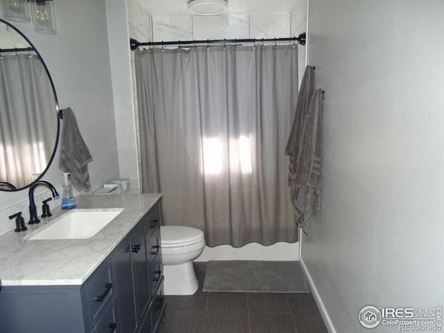 bathroom featuring toilet, baseboards, shower / bath combo with shower curtain, and vanity