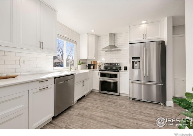 kitchen featuring a sink, white cabinetry, appliances with stainless steel finishes, decorative backsplash, and wall chimney exhaust hood