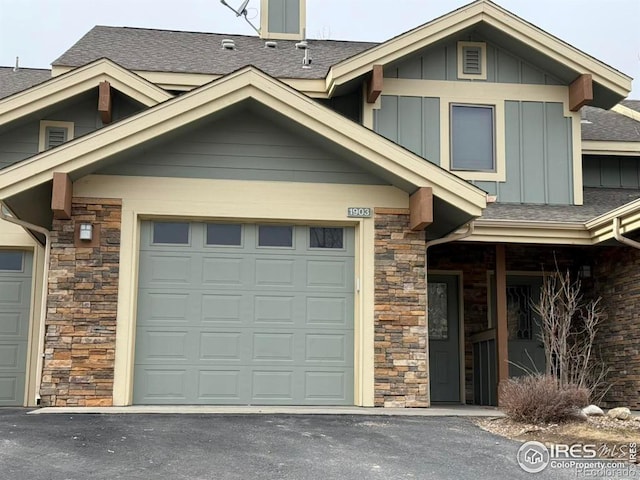 view of front of property featuring a garage, stone siding, board and batten siding, and driveway