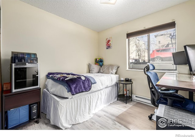 bedroom with a baseboard radiator, light wood-style flooring, and a textured ceiling