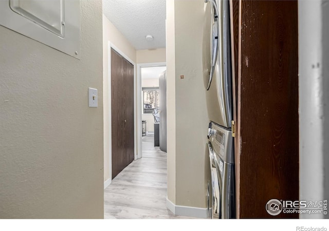 hallway featuring light wood-style floors, a textured wall, a textured ceiling, and baseboards