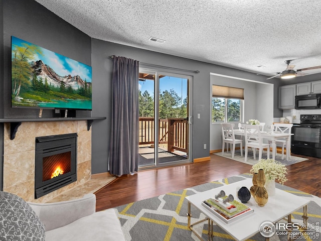 living room featuring baseboards, visible vents, a tile fireplace, wood finished floors, and a textured ceiling