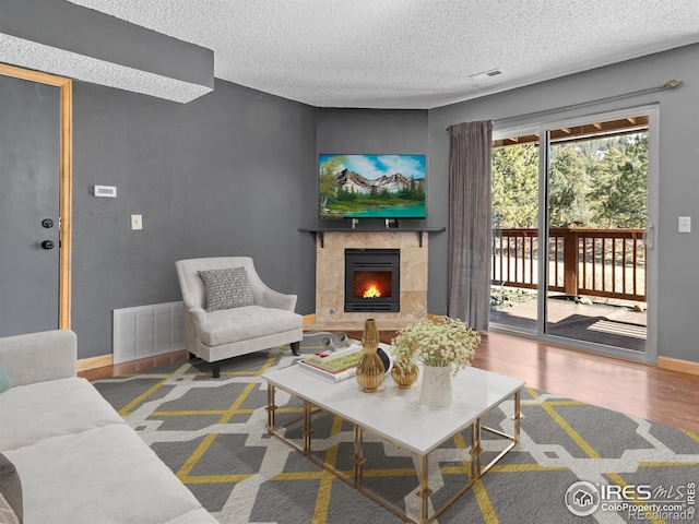 living room with a tiled fireplace, wood finished floors, visible vents, and baseboards