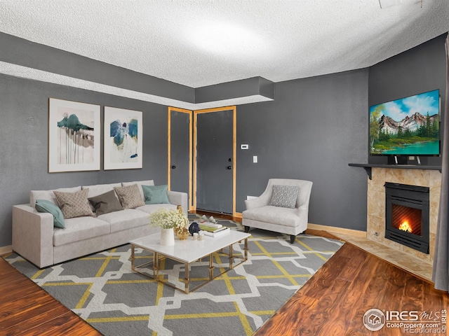 living room featuring a textured ceiling, a tiled fireplace, baseboards, and wood finished floors