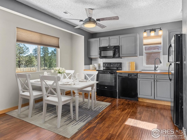 kitchen featuring gray cabinetry, dark wood-type flooring, a sink, a wealth of natural light, and black appliances