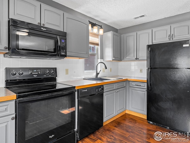 kitchen featuring dark wood-style flooring, gray cabinets, visible vents, a sink, and black appliances