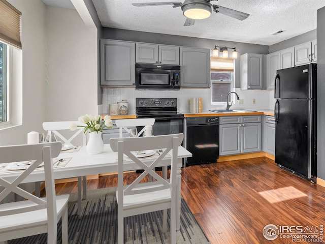 kitchen featuring dark wood-style flooring, gray cabinetry, black appliances, wooden counters, and a sink