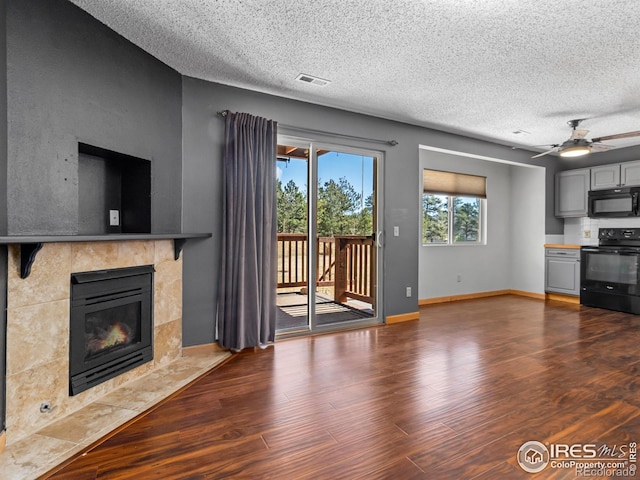 unfurnished living room with baseboards, visible vents, a tiled fireplace, dark wood-type flooring, and a textured ceiling