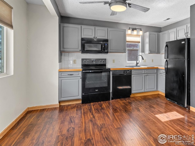 kitchen featuring gray cabinetry, a sink, baseboards, dark wood-style floors, and black appliances