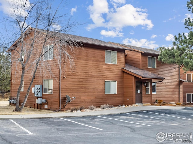 exterior space with uncovered parking and roof with shingles