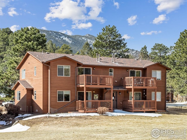 rear view of house with a balcony, a shingled roof, a mountain view, and a lawn