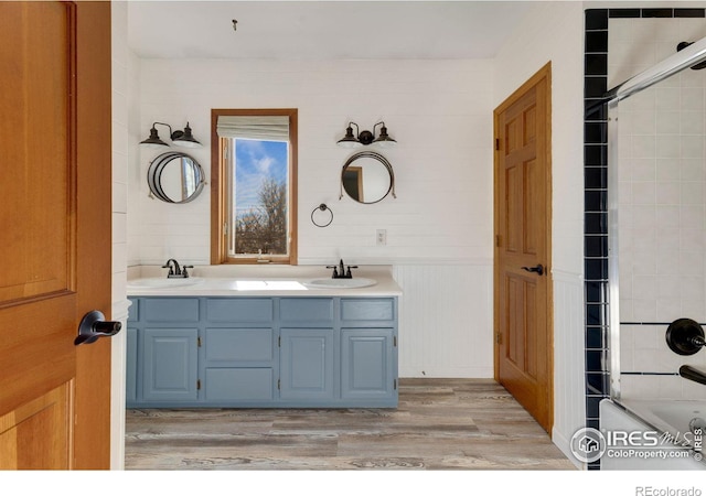 full bath featuring wood finished floors, a sink, shower / bathing tub combination, and double vanity