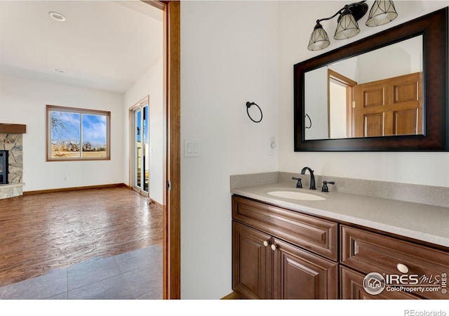 bathroom with baseboards, a stone fireplace, vanity, and wood finished floors