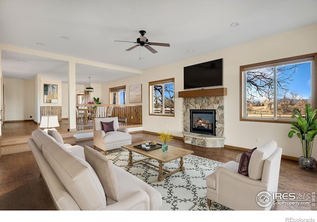 living area featuring a ceiling fan, a fireplace, baseboards, and wood finished floors