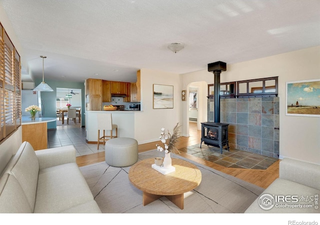 living room with arched walkways, light wood-style flooring, a wood stove, and baseboards