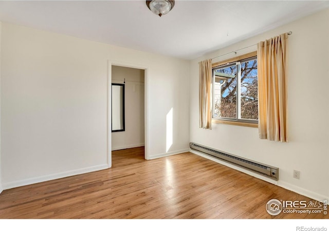 spare room featuring a baseboard heating unit, baseboards, and wood finished floors