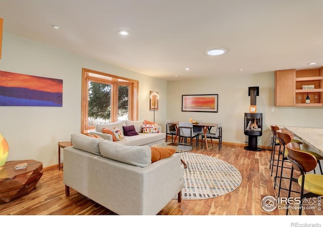 living area featuring baseboards, recessed lighting, a wood stove, and light wood-style floors