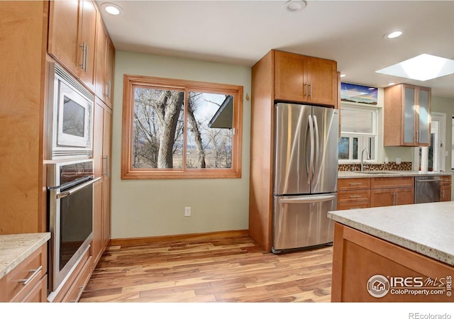 kitchen featuring glass insert cabinets, brown cabinets, appliances with stainless steel finishes, light countertops, and a sink