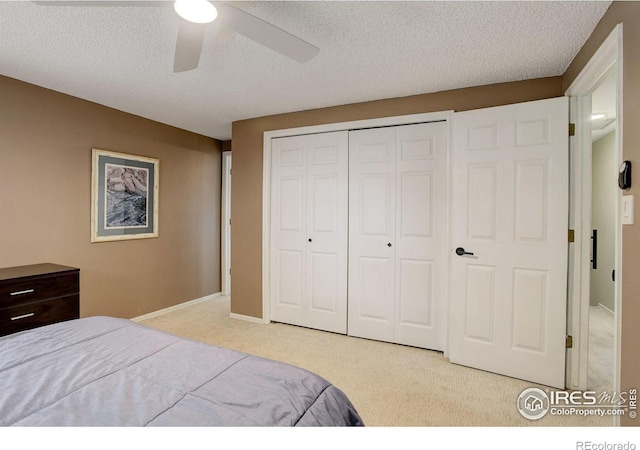 bedroom with a textured ceiling, light colored carpet, a ceiling fan, baseboards, and a closet