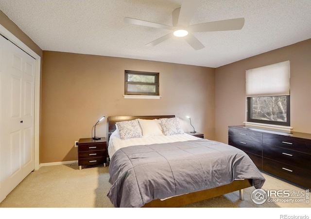 bedroom with a closet, light carpet, ceiling fan, a textured ceiling, and baseboards