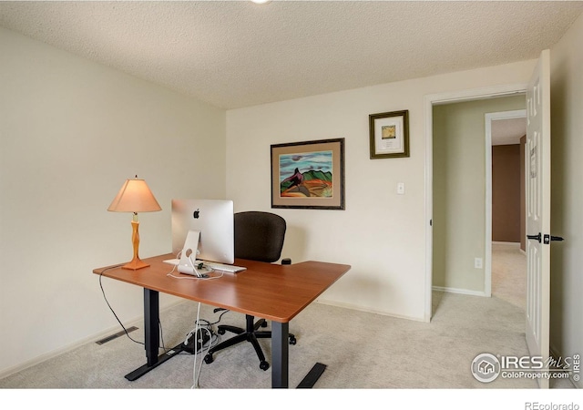 office featuring baseboards, a textured ceiling, and light colored carpet