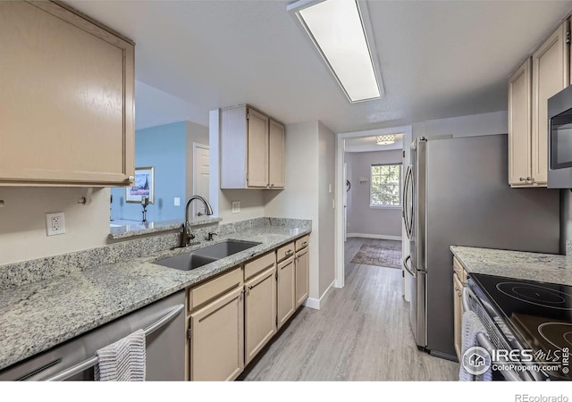 kitchen featuring a sink, baseboards, appliances with stainless steel finishes, light stone countertops, and light wood finished floors