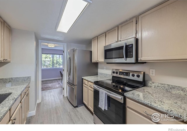 kitchen featuring light wood finished floors, baseboards, light stone counters, and stainless steel appliances