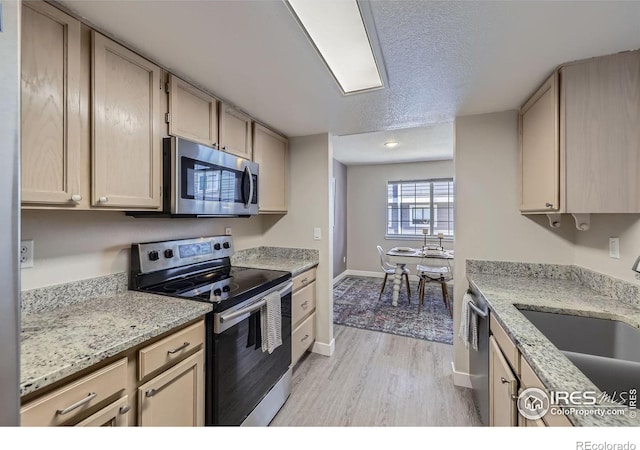 kitchen with baseboards, stainless steel appliances, a textured ceiling, light wood-style floors, and a sink