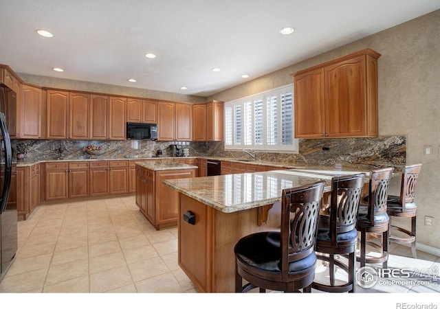 kitchen with light stone counters, a center island, a breakfast bar area, brown cabinetry, and black appliances