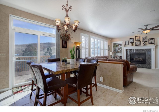 dining room featuring light tile patterned floors, ceiling fan with notable chandelier, light carpet, baseboards, and a glass covered fireplace