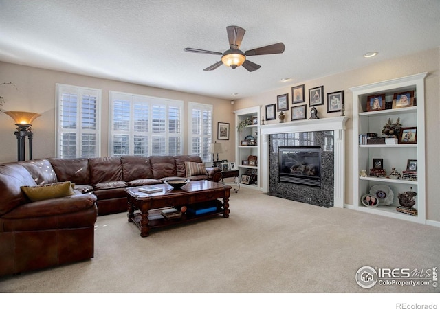 carpeted living area featuring a textured ceiling, built in shelves, a ceiling fan, and a tiled fireplace