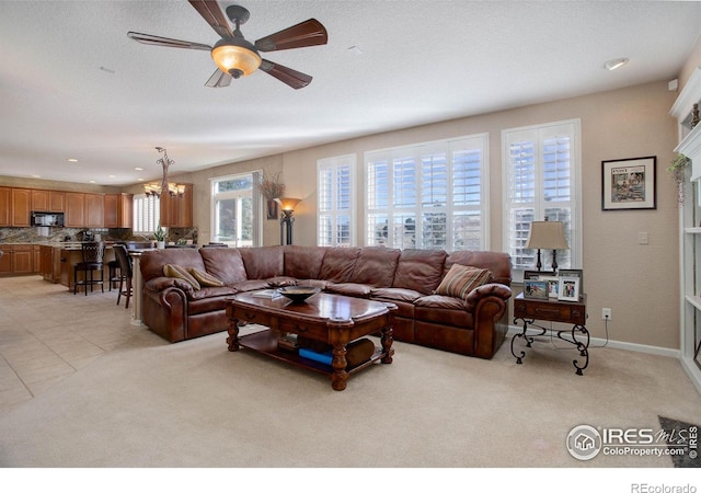 living area featuring light tile patterned floors, light colored carpet, baseboards, and ceiling fan with notable chandelier