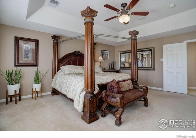 bedroom with light carpet, visible vents, baseboards, a tray ceiling, and ornate columns