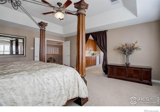 bedroom featuring a tray ceiling, light colored carpet, and ornate columns