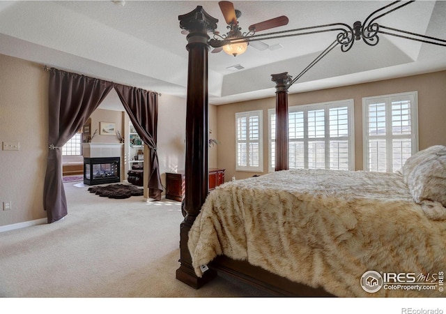 bedroom with carpet floors, visible vents, baseboards, a tiled fireplace, and a raised ceiling