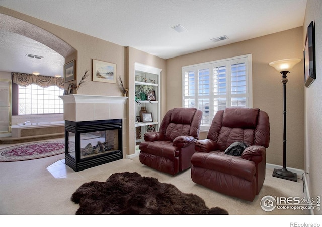 carpeted living room with a fireplace, visible vents, arched walkways, and a textured ceiling