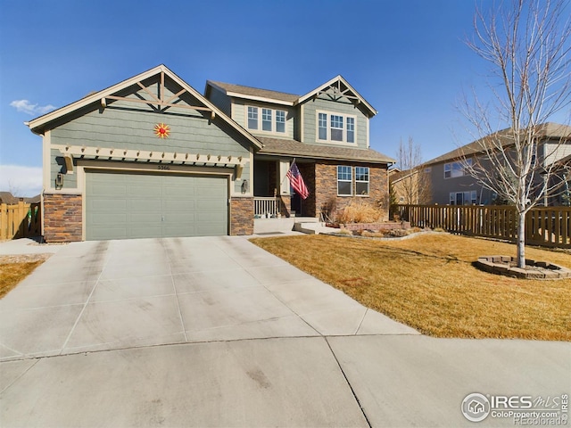 craftsman-style home with stone siding, concrete driveway, fence, and a front lawn