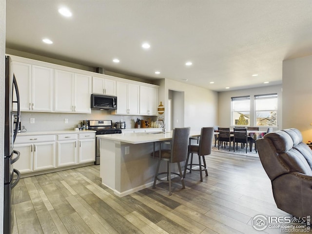 kitchen featuring a kitchen island with sink, a breakfast bar, white cabinetry, light countertops, and appliances with stainless steel finishes